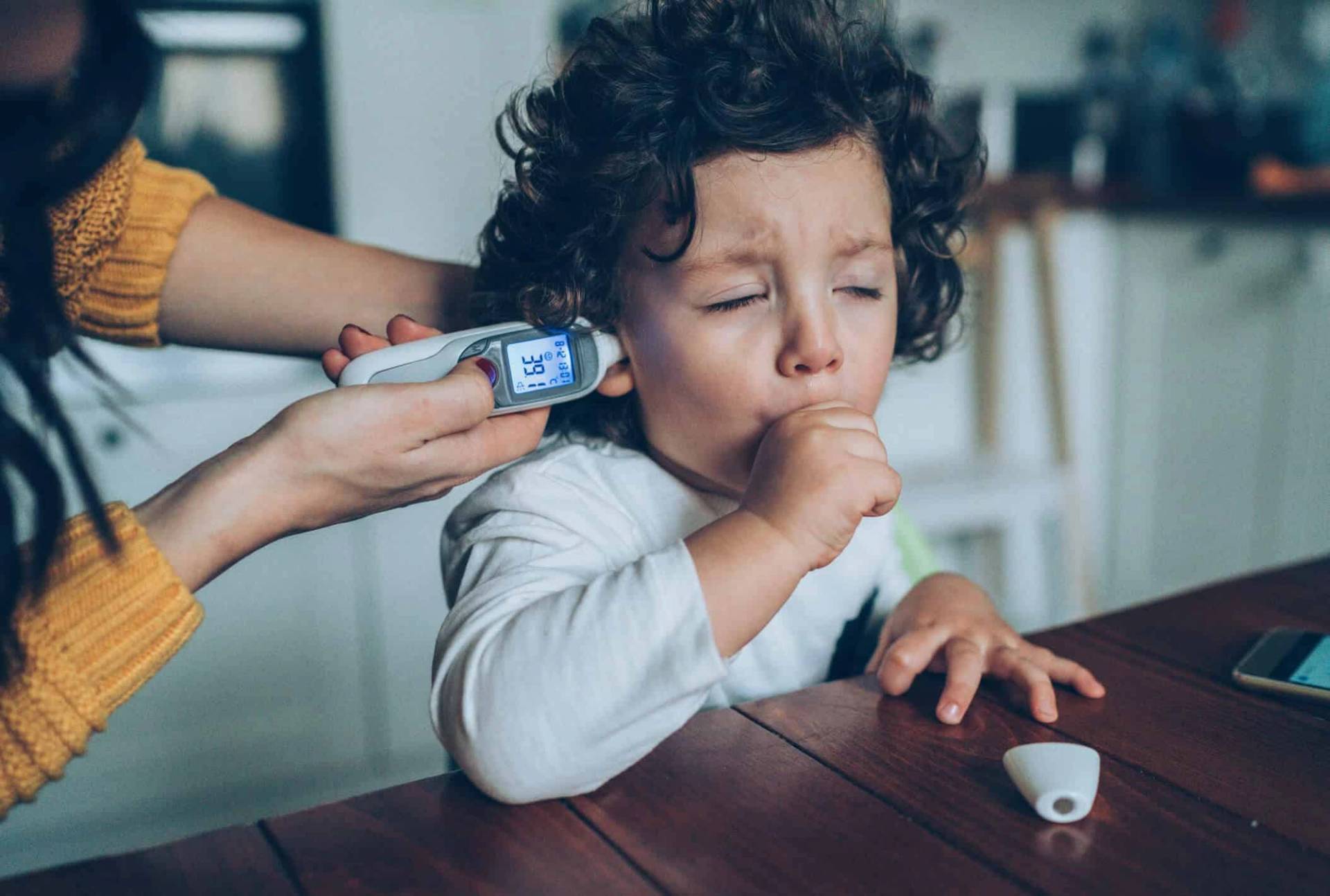 Enfant toussant pendant une prise de température à l’oreille.