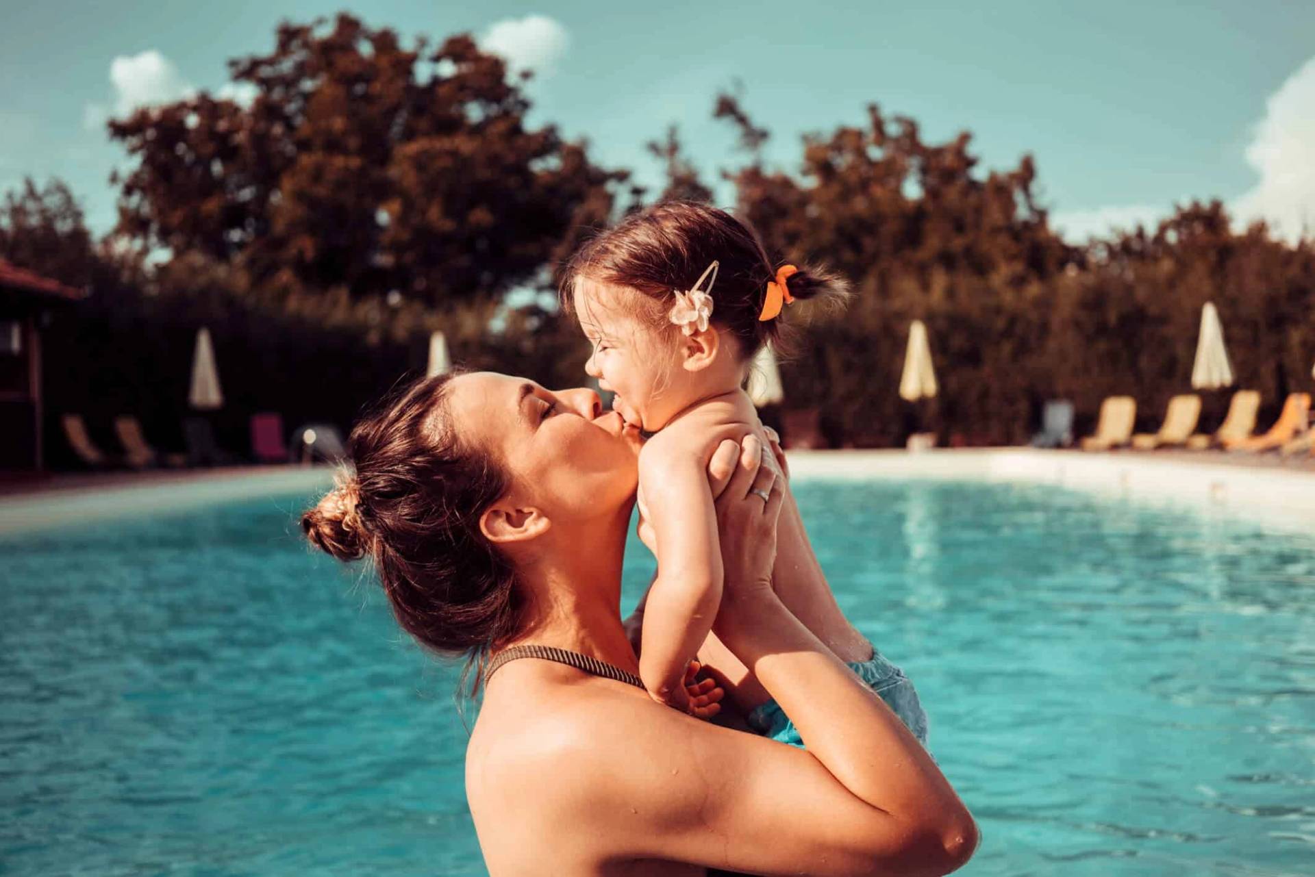 Adulte portant un enfant au bord d’une piscine.