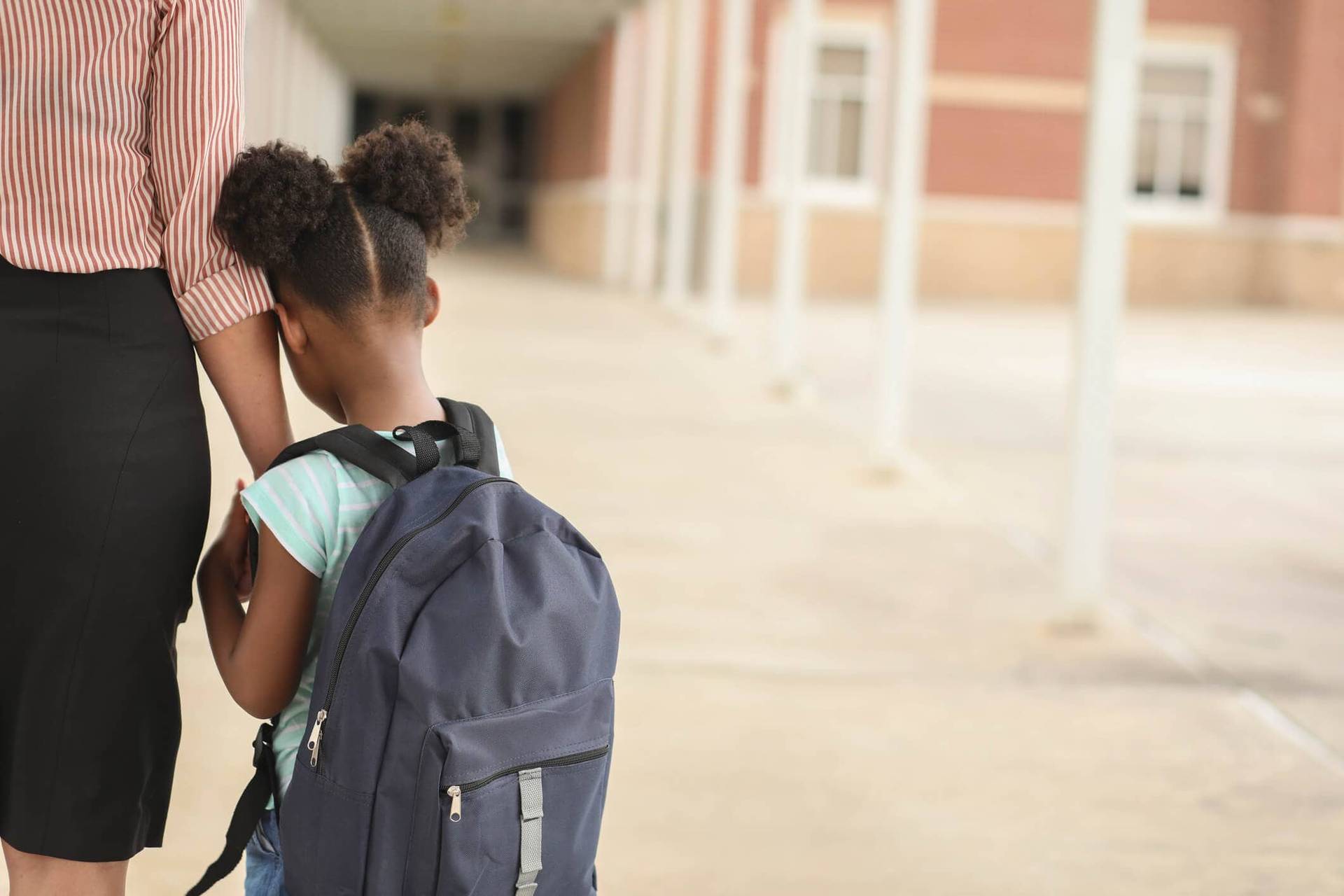 Enfant avec un cartable se tenant contre un adulte devant une école.