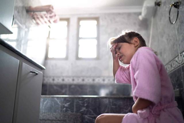 Enfant en peignoir assis aux toilettes.