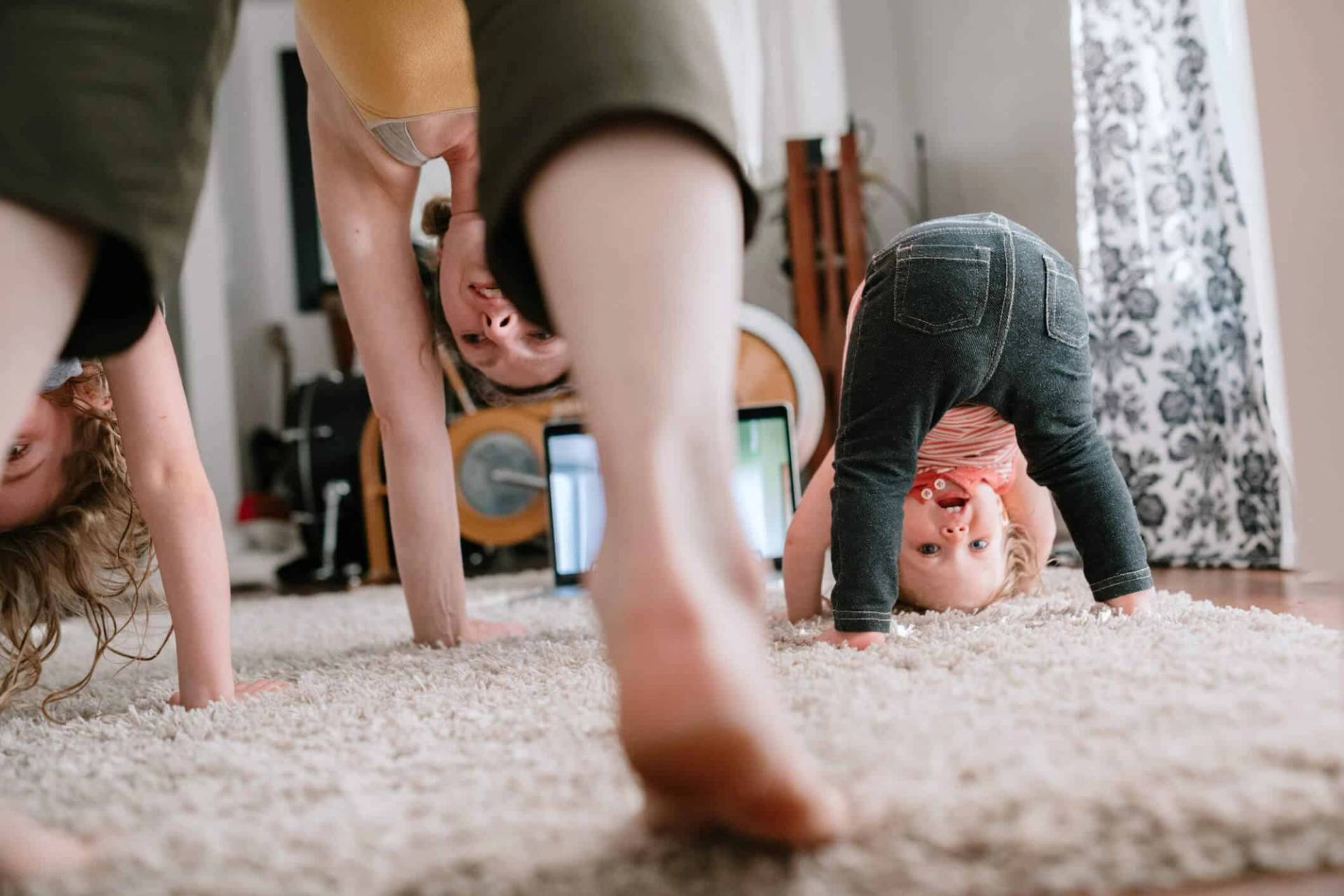 Un adulte et deux jeunes enfants jouent la tête en bas sur le tapis du salon.