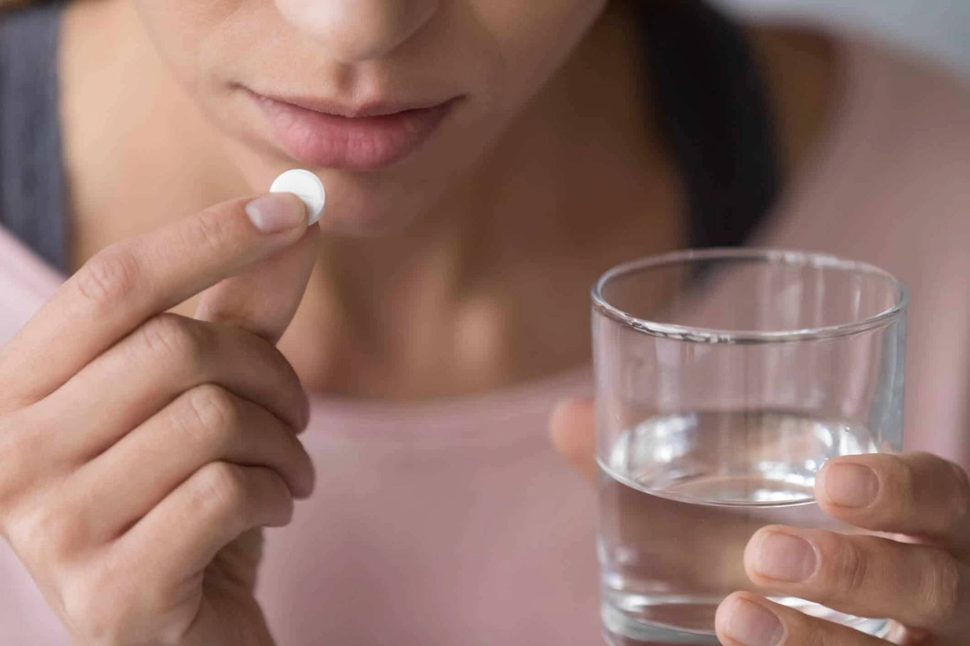 Femme prenant un comprimé avec de l’eau.