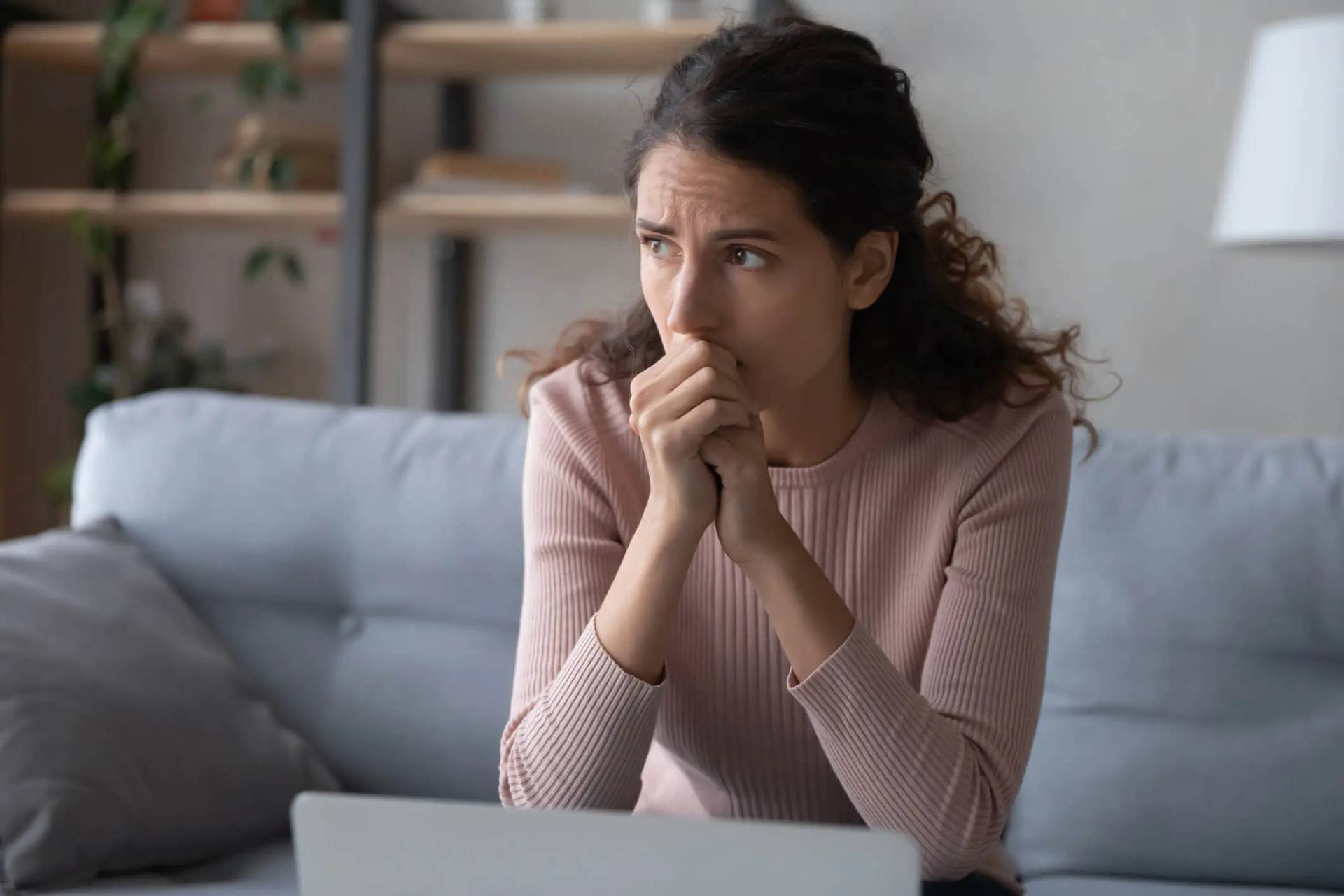Femme préoccupée sur un canapé devant un ordinateur.