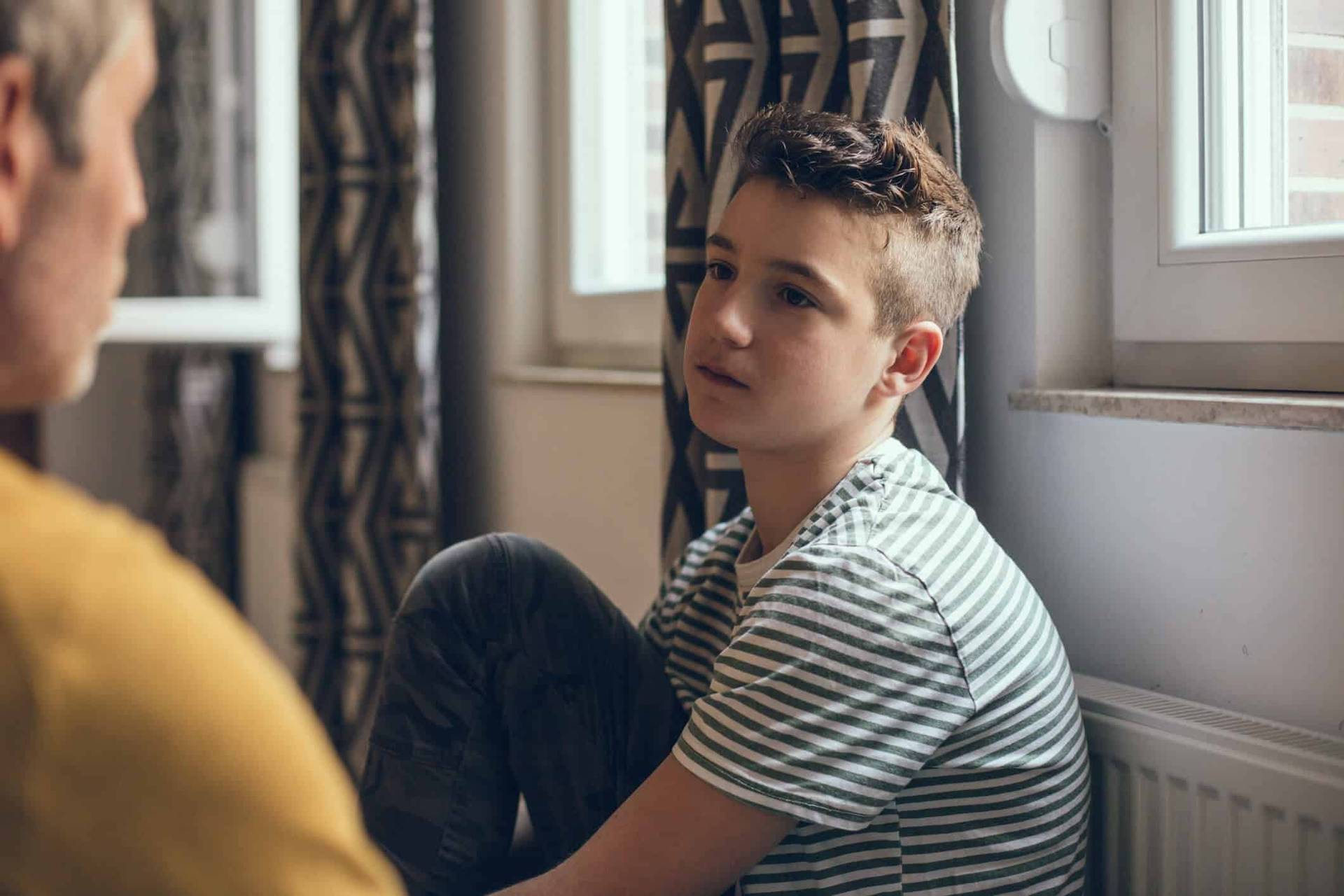 Enfant assis près d’une fenêtre face à un adulte.