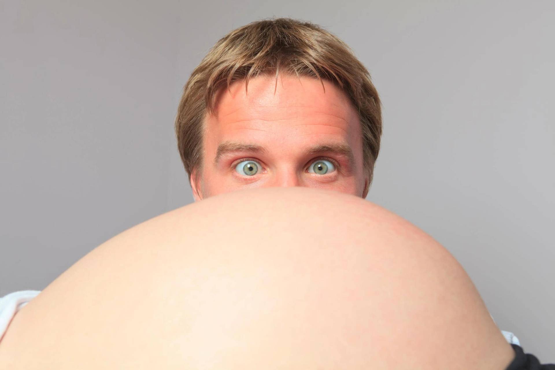 Homme regardant par-dessus un ventre de femme enceinte.