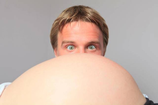 Homme regardant par-dessus un ventre de femme enceinte.