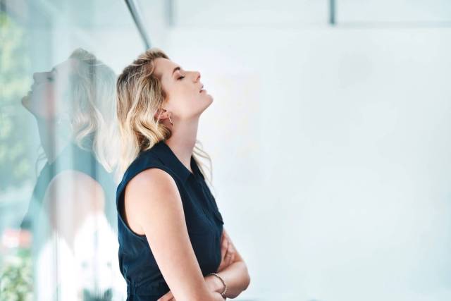 Femme près d’une vitre, les bras croisés devant le ventre.