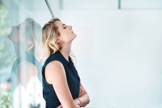 Femme près d’une vitre, les bras croisés devant le ventre.