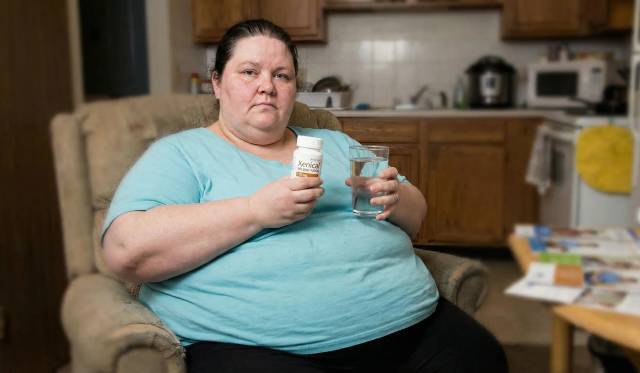 Femme dans un fauteuil tenant un flacon et un verre d’eau.