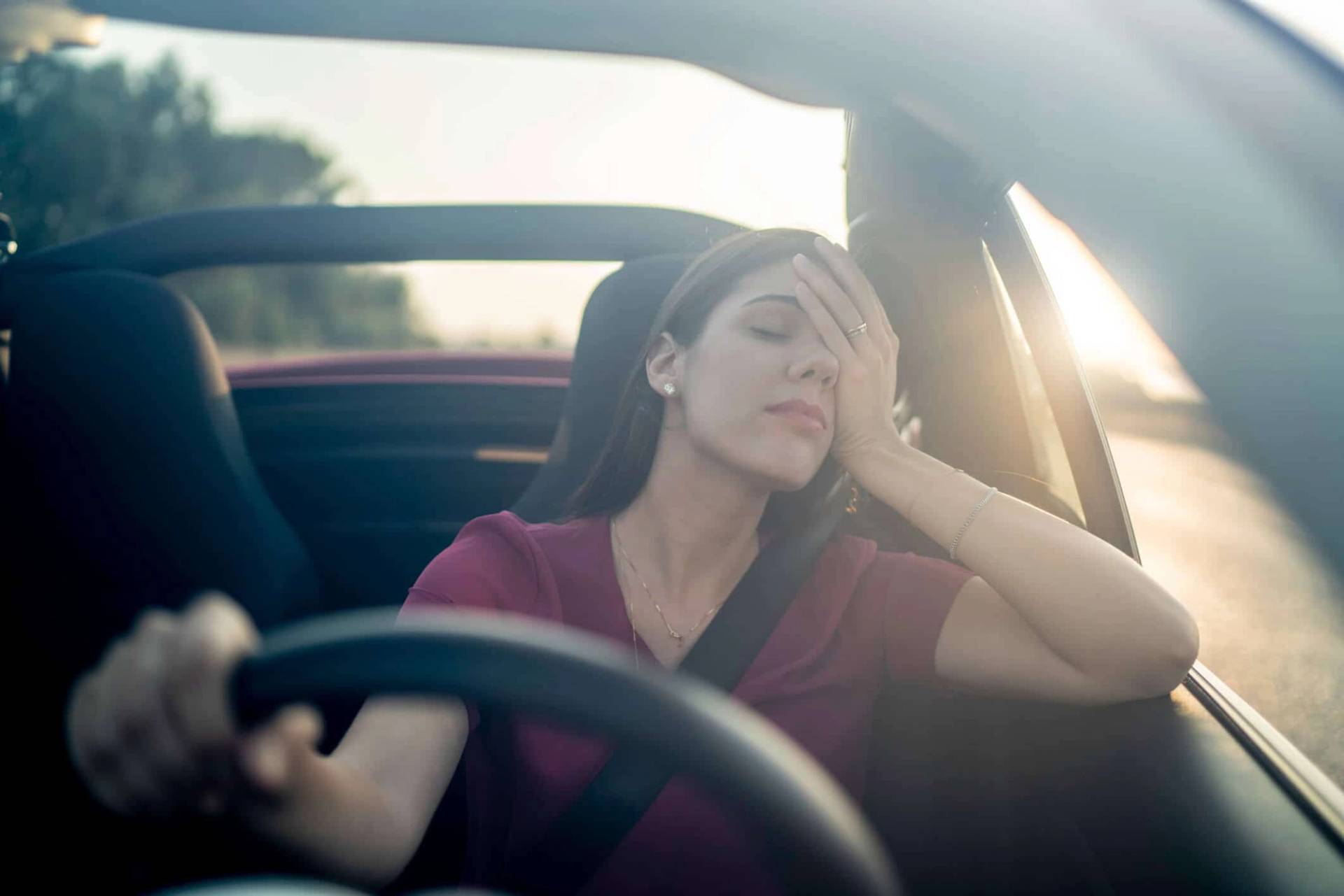 Femme au volant, la main au front.