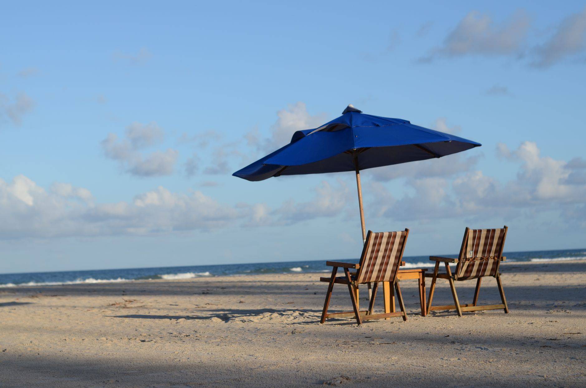 Deux chaises de plage sous un parasol face à la mer.