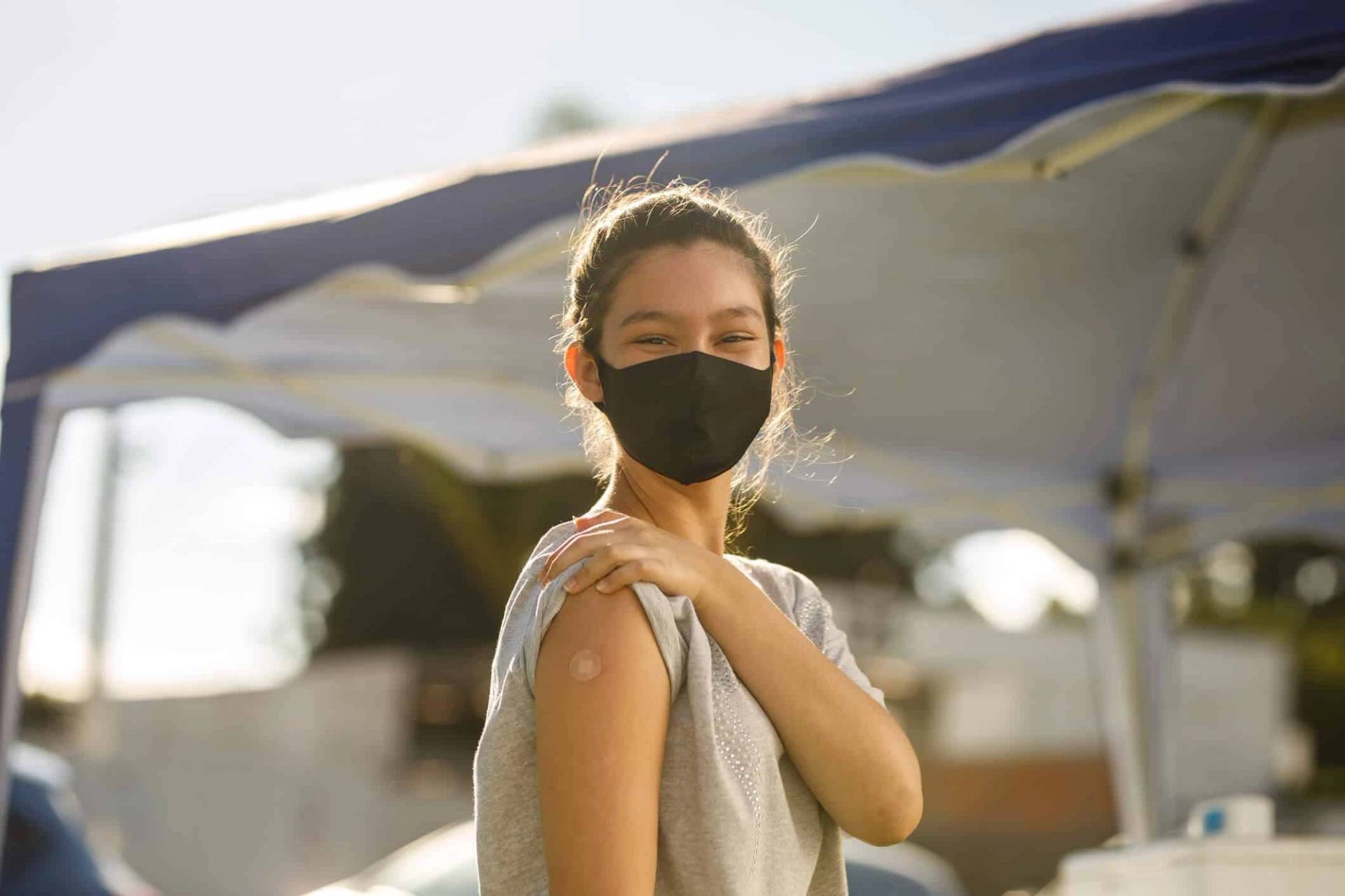 Femme masquée montrant son bras portant un pansement.