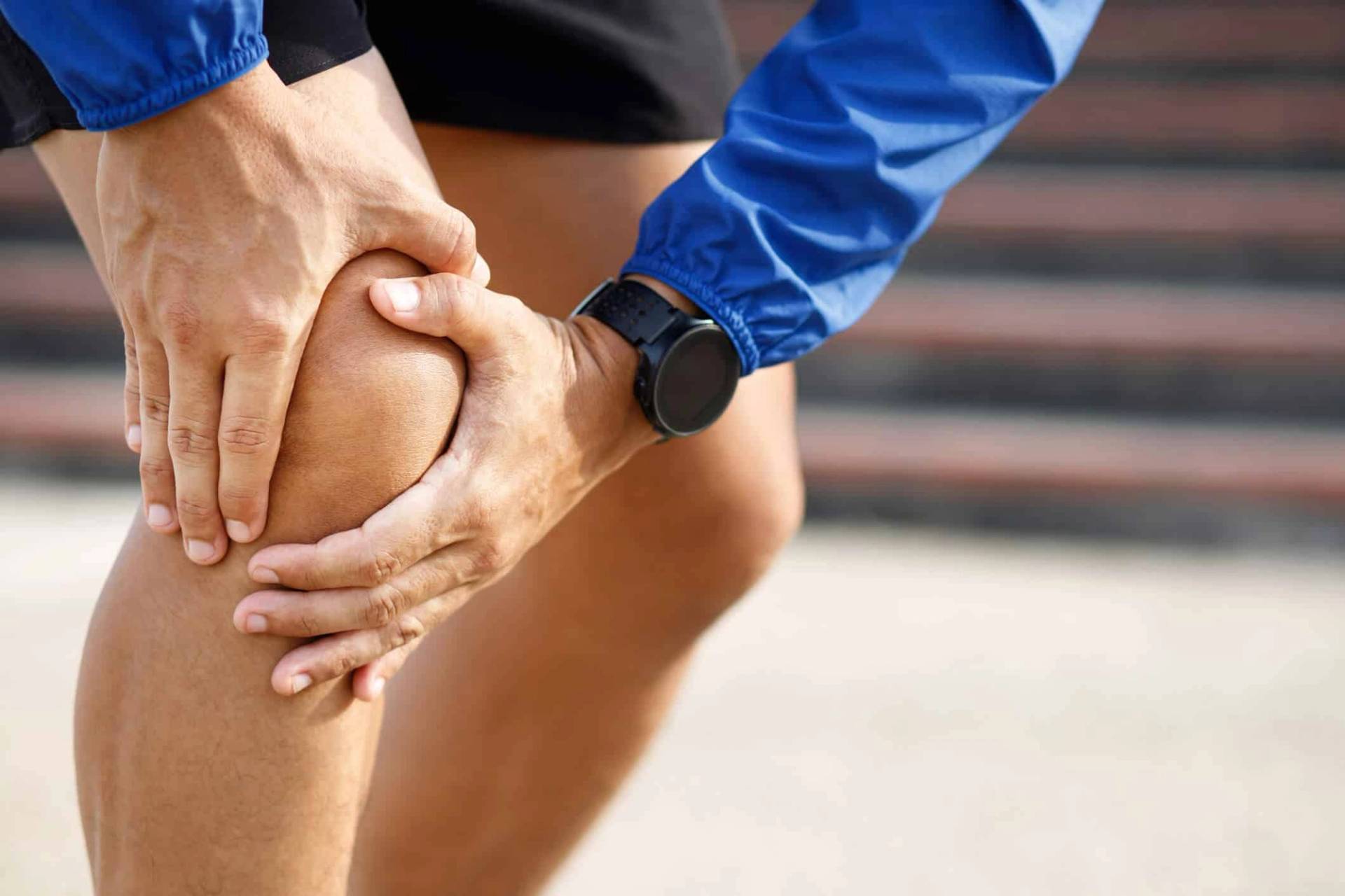 Un sportif se tient le genou avec les deux mains.