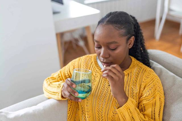 Une femme prend un comprimé avec un verre d'eau.