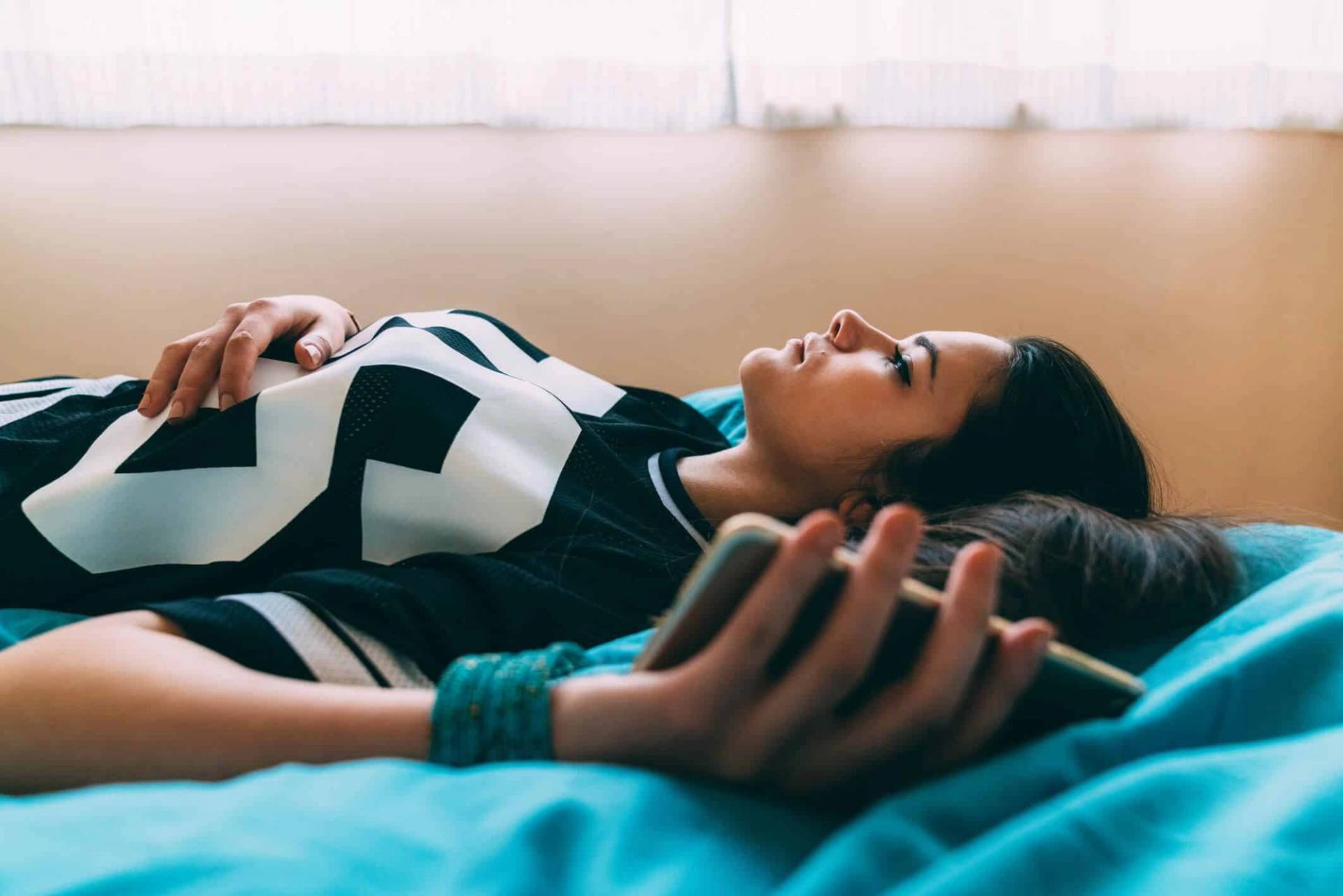Une femme reste allongée sur son lit, le regard tourné vers le plafond.