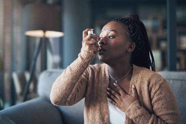 Une femme utilise un inhalateur, une main posée sur la poitrine.