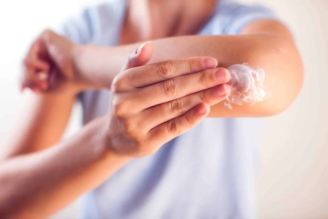 Une personne applique une crème sur son coude.