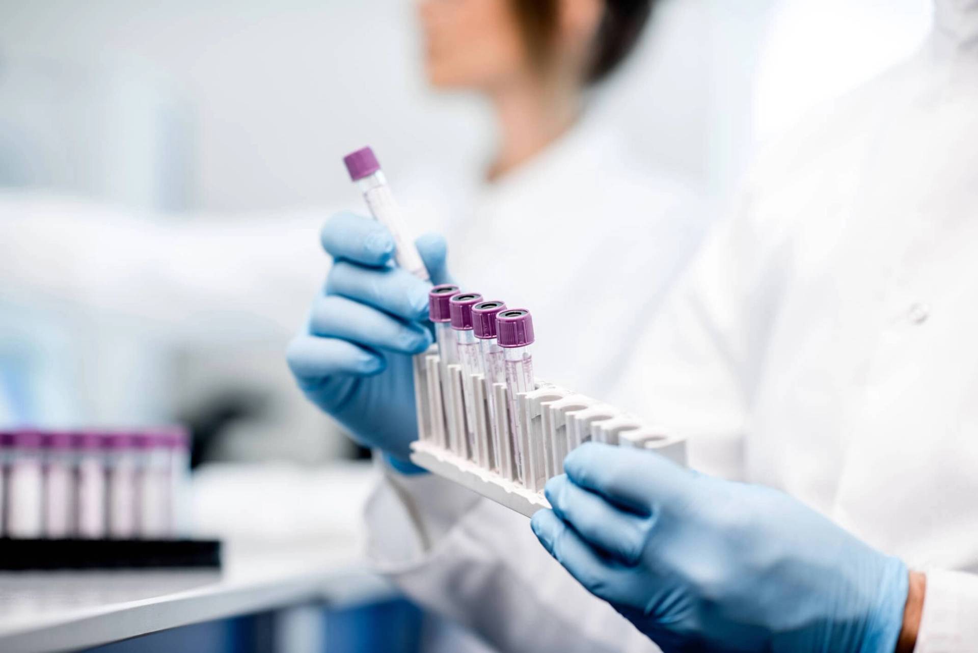 Une personne portant des gants manipule des tubes de prélèvement au laboratoire.