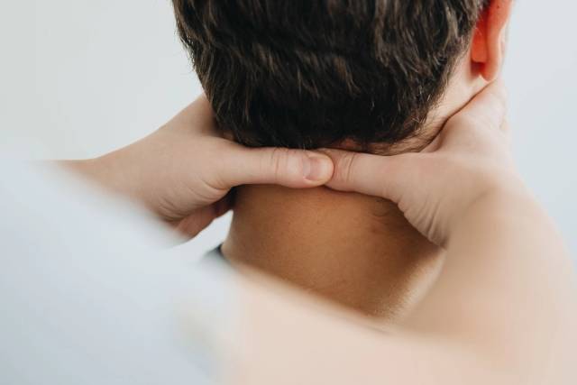 Mains massant la nuque d’une personne vue de dos.