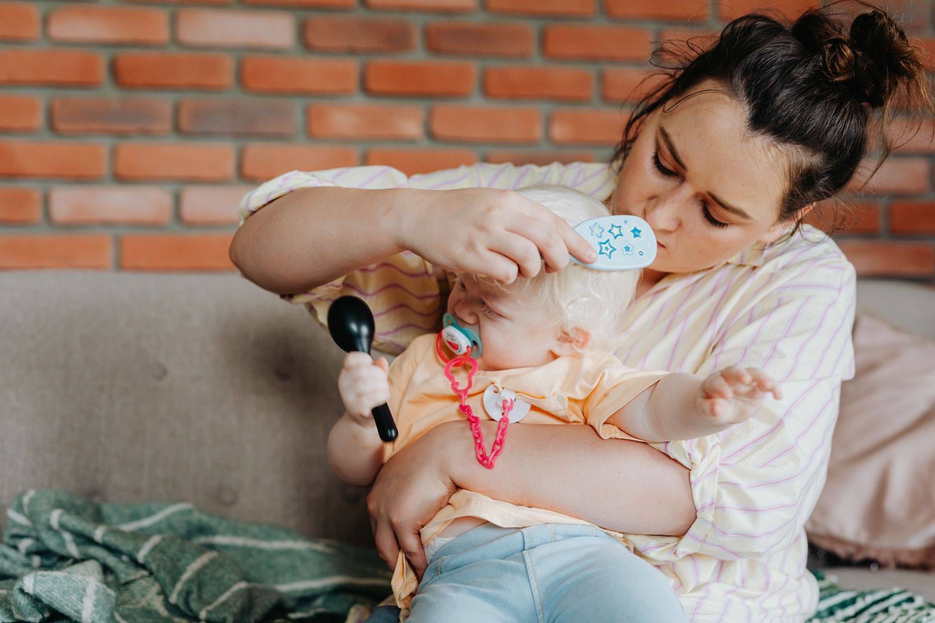Une mère peigne doucement les cheveux de son bébé tout en tenant l'enfant dans un cadre intérieur confortable