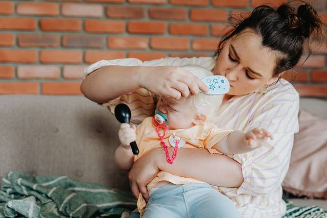Une mère peigne doucement les cheveux de son bébé tout en tenant l'enfant dans un cadre intérieur confortable