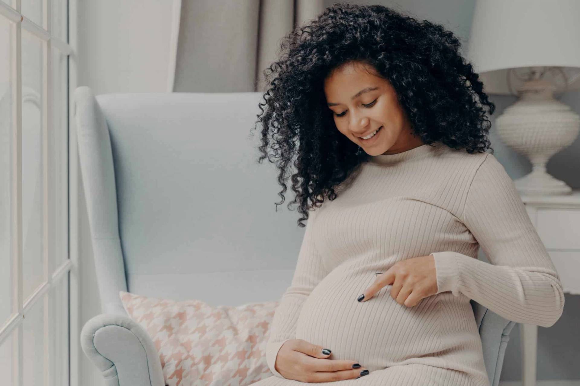Une femme enceinte assise dans un fauteuil pose les mains sur son ventre.