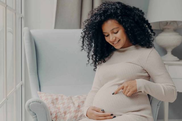 Une femme enceinte assise dans un fauteuil pose les mains sur son ventre.