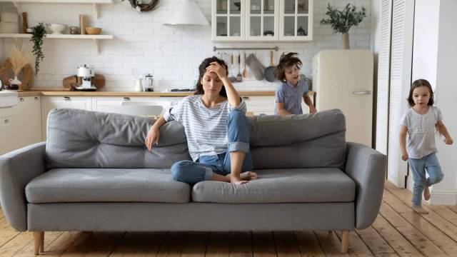 Femme assise sur un canapé, une main sur le front, avec plusieurs personnes autour d’elle.