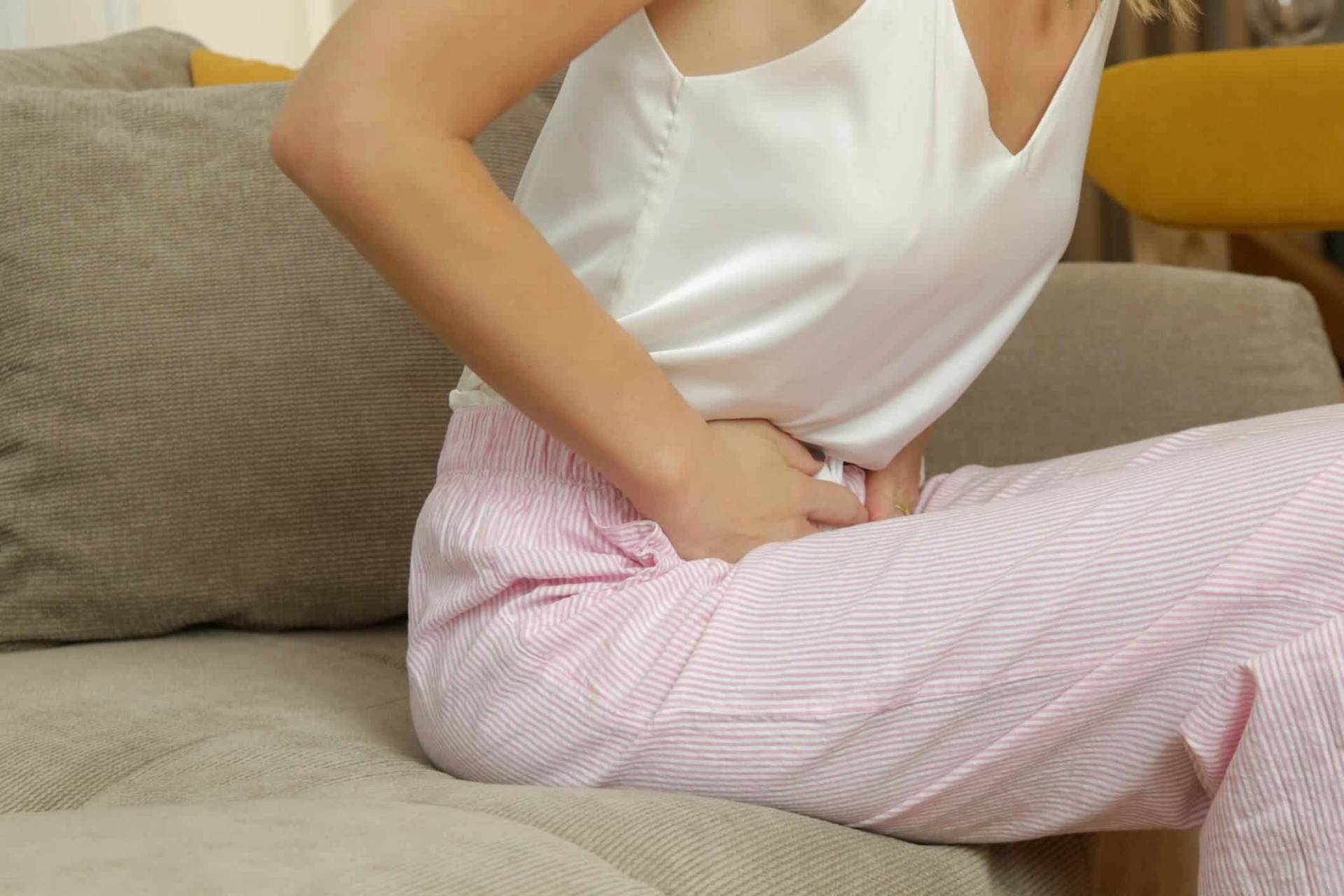 Une femme assise sur un canapé se tient le ventre.