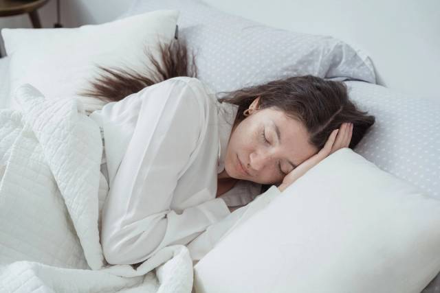 Une femme sereine repose confortablement dans un lit avec des oreillers et des couvertures doux, embrassant la