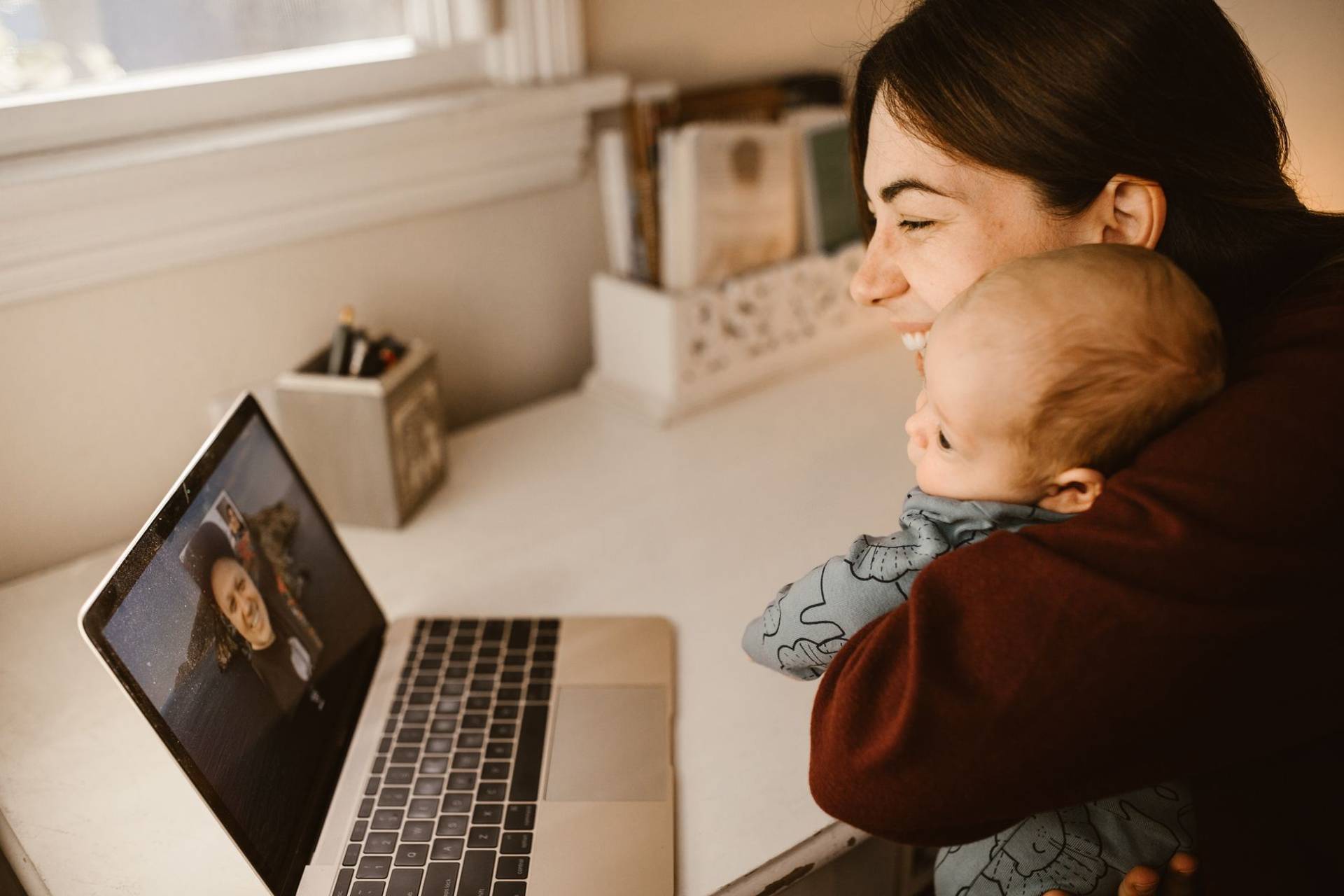 Adulte tenant un bébé et échangeant en vidéo sur un ordinateur portable.