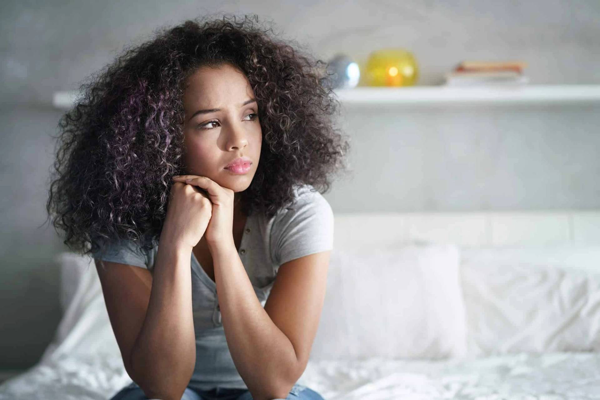 Une femme assise sur un lit paraît préoccupée.