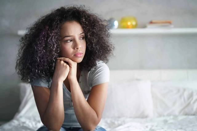 Une femme assise sur un lit paraît préoccupée.