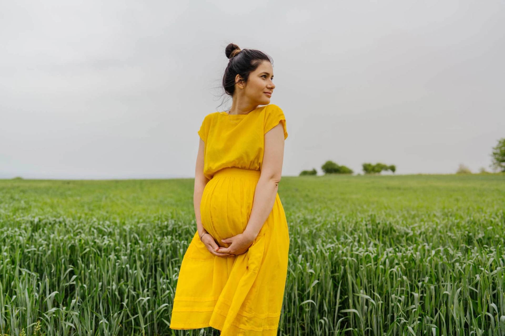 Une femme enceinte en robe jaune se tient dans un champ.