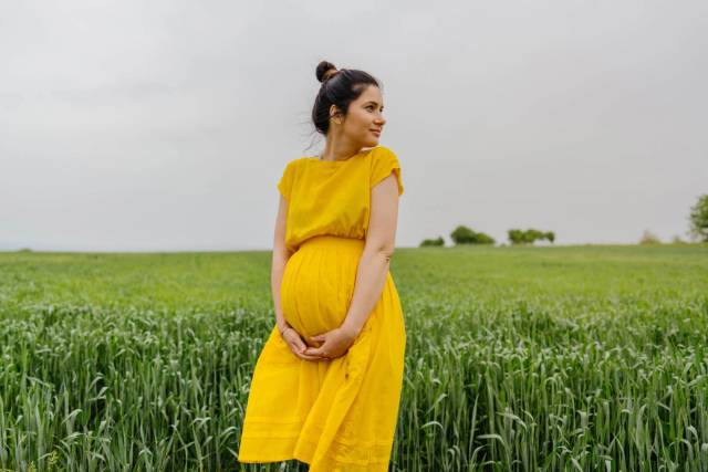 Une femme enceinte en robe jaune se tient dans un champ.