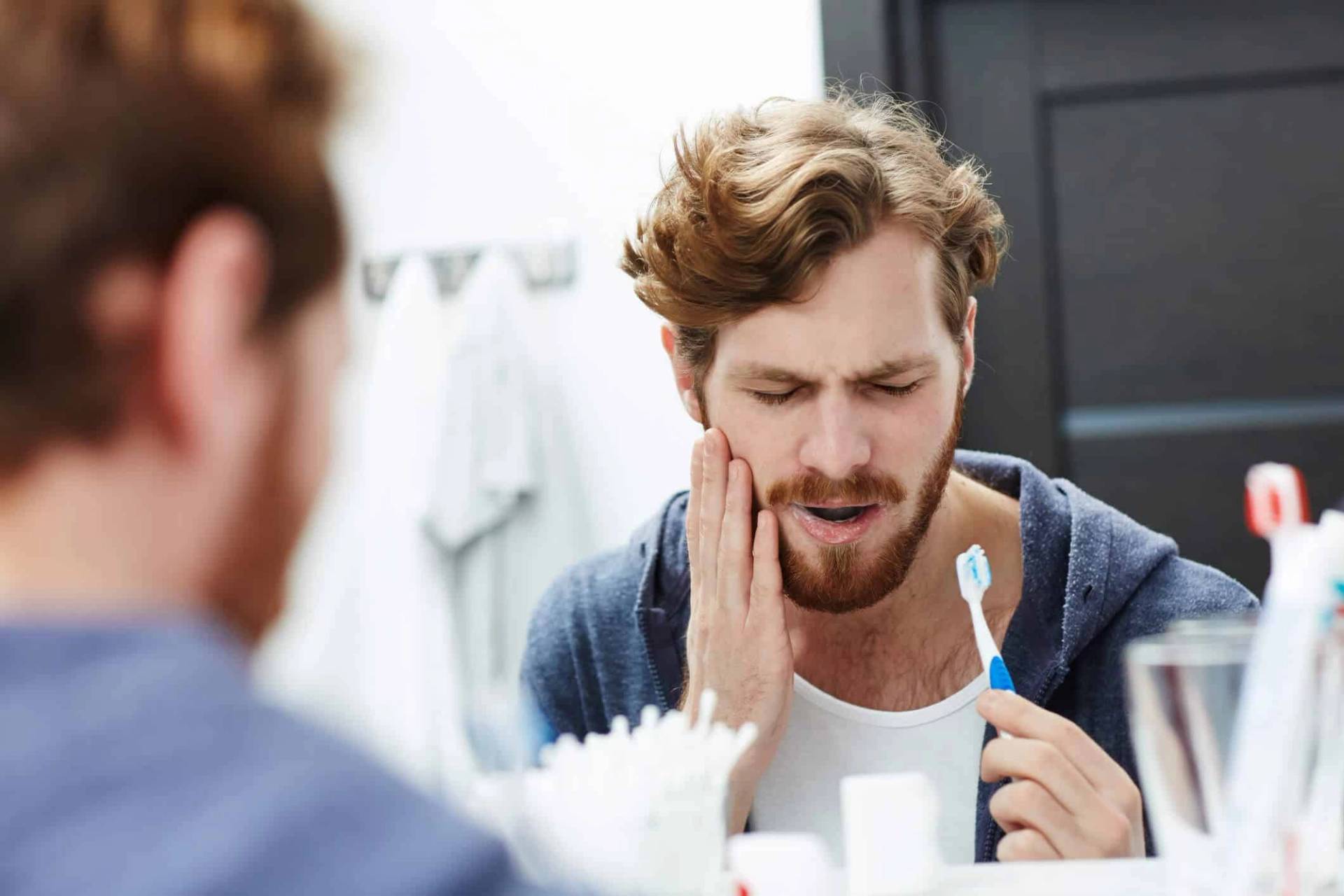 Un homme se tient la joue devant un miroir, une brosse à dents à la main.