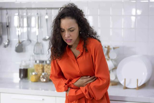 Une femme debout dans une cuisine se tient le ventre.