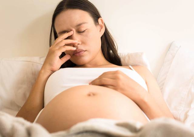 Une femme enceinte allongée pose une main sur son front.