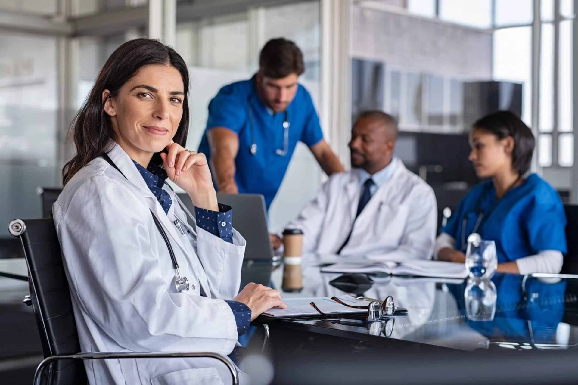 Femme au premier plan, avec un groupe en tenue médicale en réunion derrière elle.