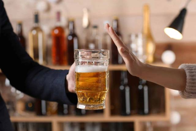 Une personne refuse un verre de bière en levant la main.