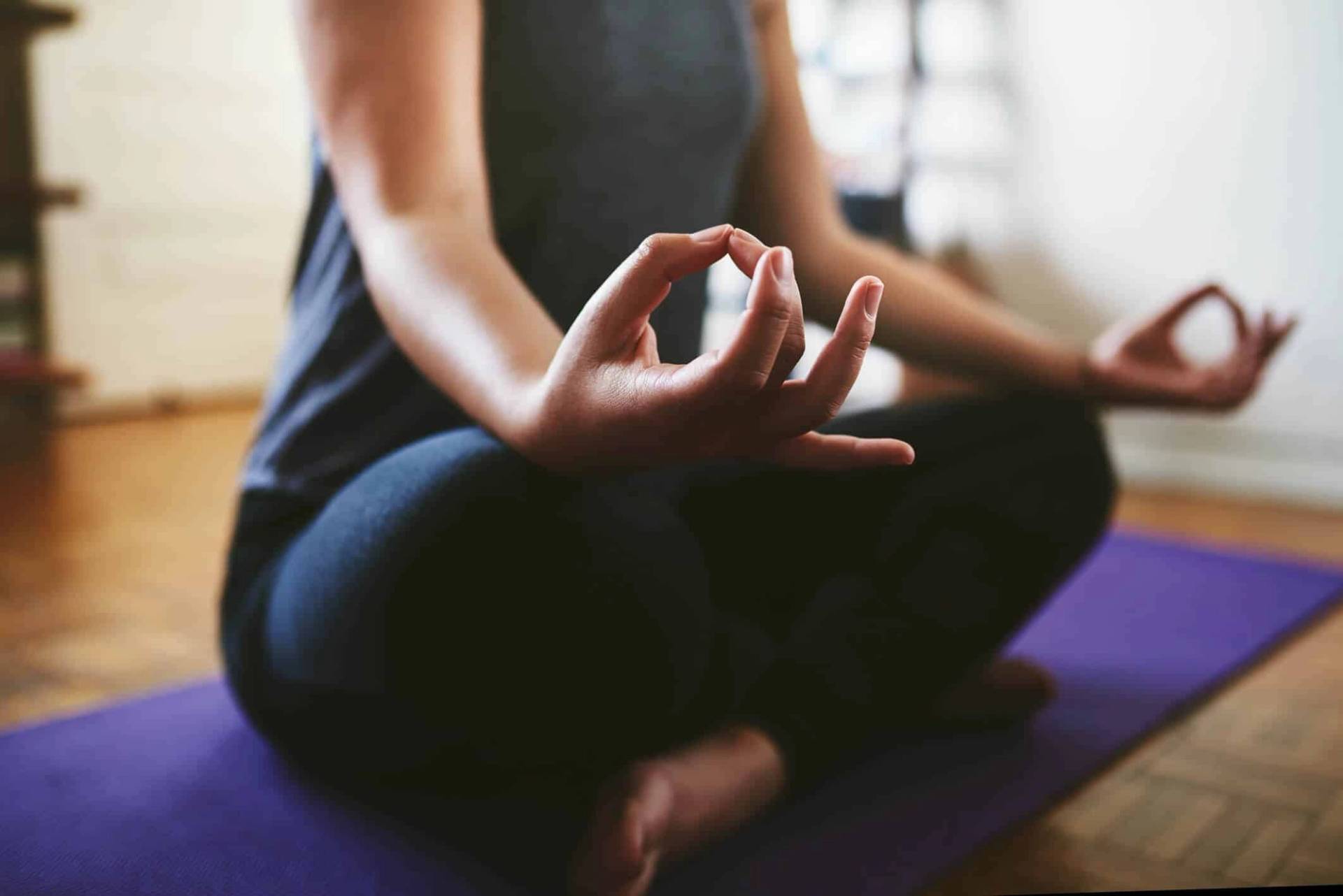 Une personne assise en tailleur sur un tapis de yoga, les mains posées sur les genoux pour méditer.