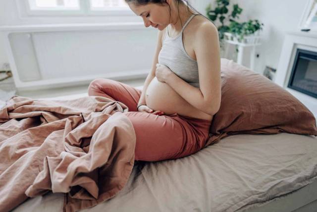 Une femme enceinte assise sur un lit regarde son ventre.