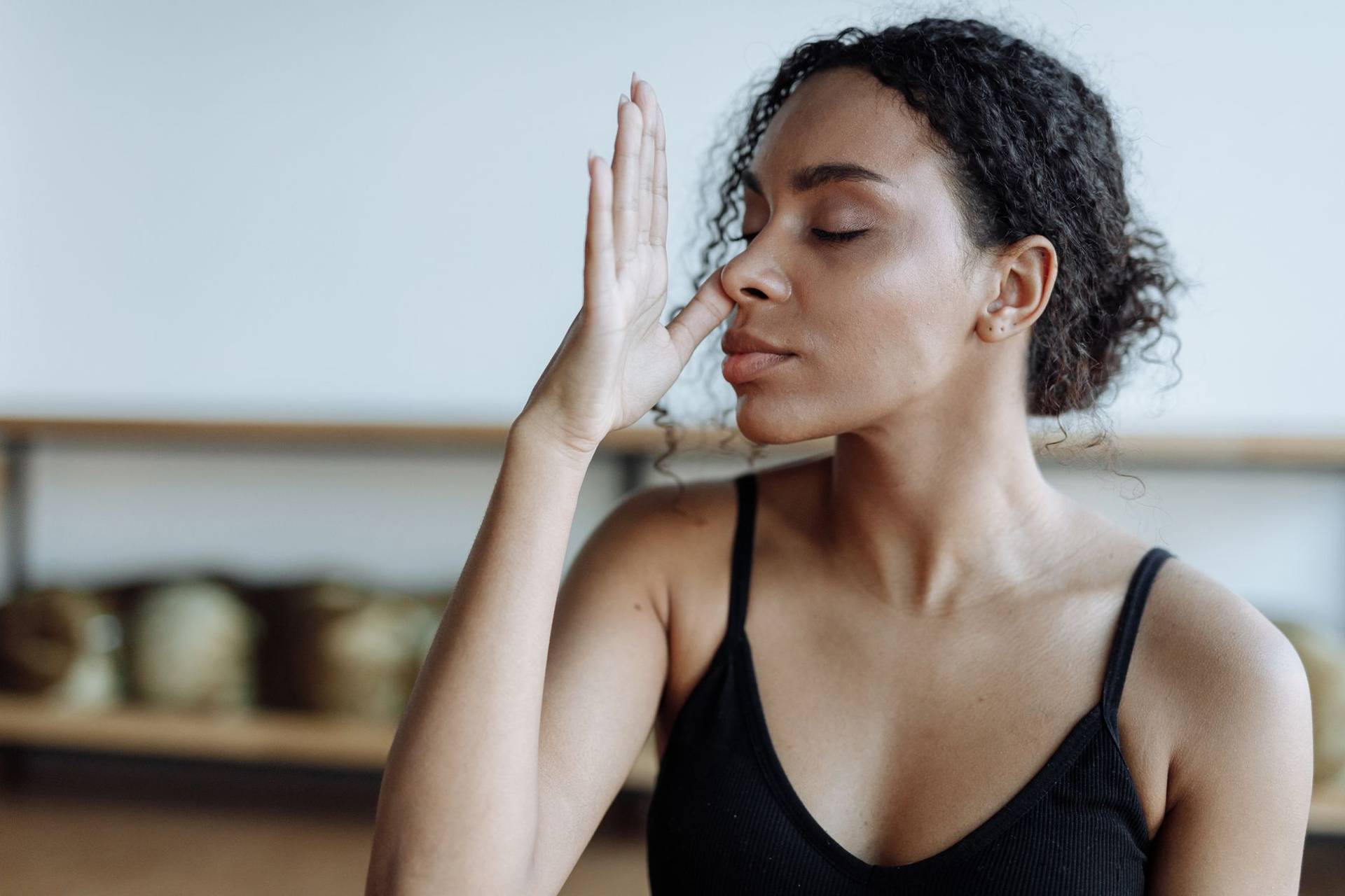 Une femme fait un exercice de respiration, les yeux fermés, une main devant le visage.