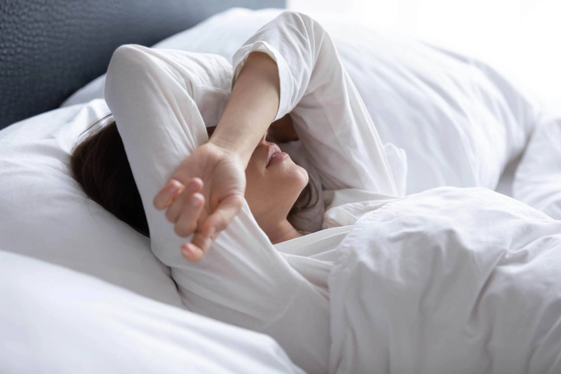 Une personne allongée dans son lit couvre son visage avec son bras.