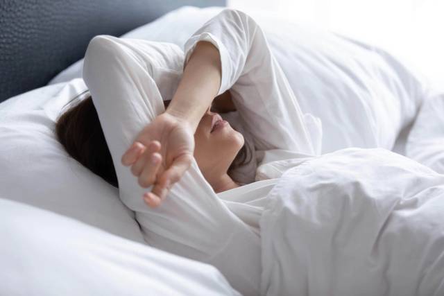 Une personne allongée dans son lit couvre son visage avec son bras.