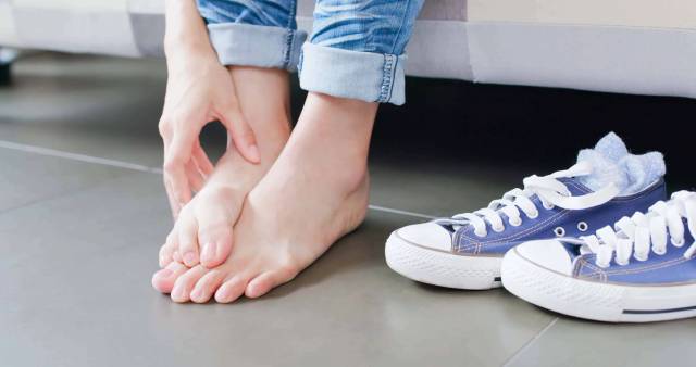 Une personne se gratte le pied près d'une paire de baskets.