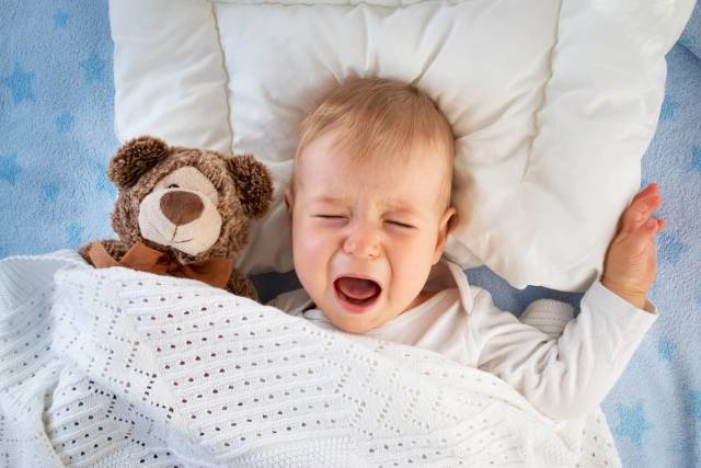 Un bébé allongé dans son lit pleure.
