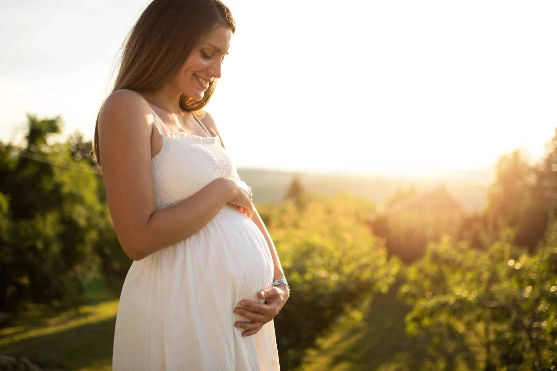Une femme enceinte pose les mains sur son ventre en extérieur.