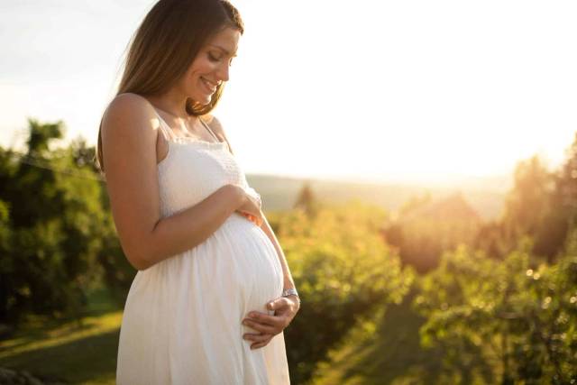 Une femme enceinte pose les mains sur son ventre en extérieur.