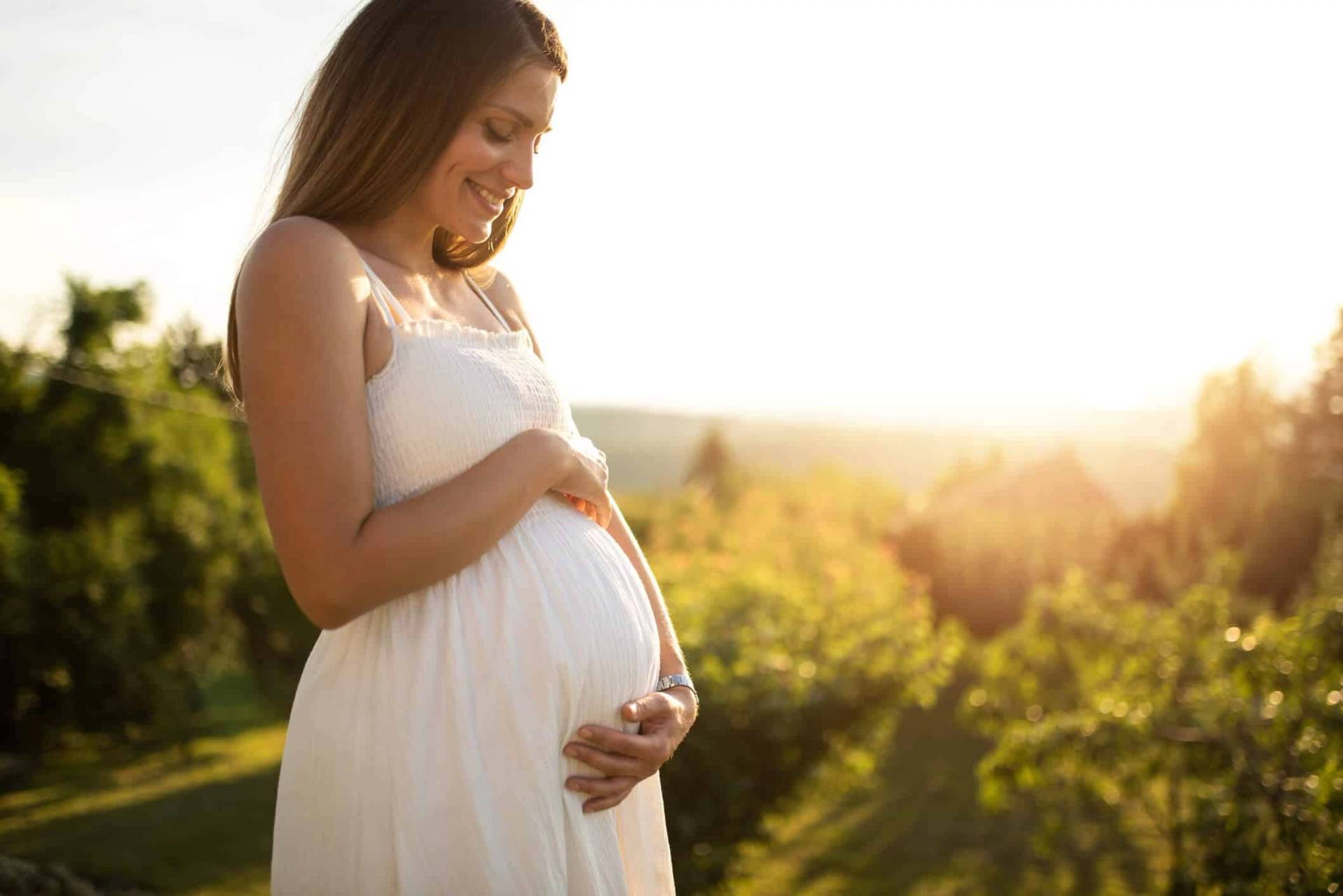 Une femme enceinte pose les mains sur son ventre en extérieur.